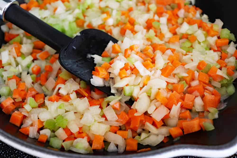 Sauteeing vegetables in a skillet with a black spatula